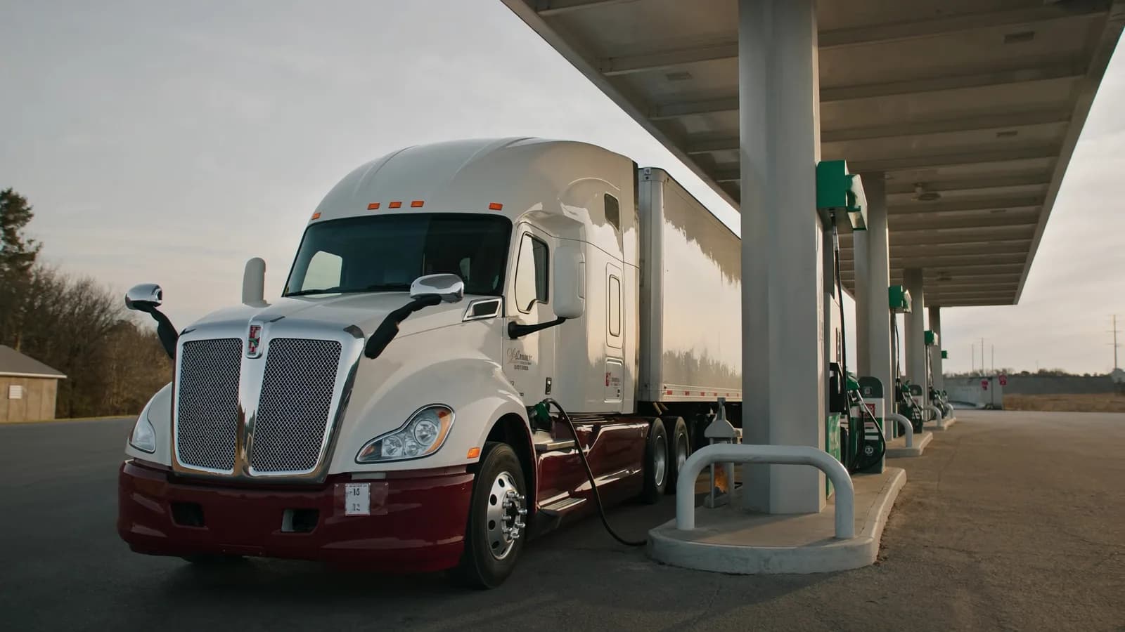 Truck fueling up at a diesel island under a truck stop canopy at dusk